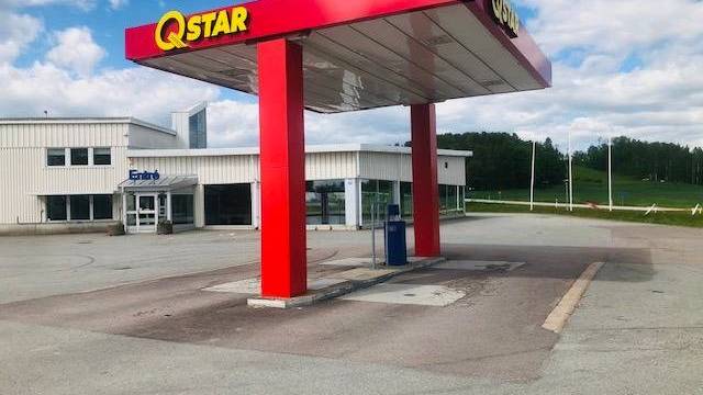 En Qstar-mack med rött skärmtak står obevakad framför en vit byggnad under en delvis molnig himmel. Området ser tomt och lugnt ut.