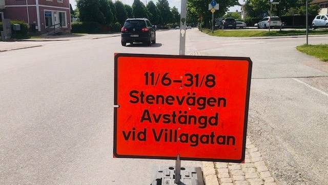 Orange vägskylt på svenska meddelar att Stenevägen är avstängd vid Villagatan från 11 juni till 31 augusti. En bil och hus syns i bakgrunden.