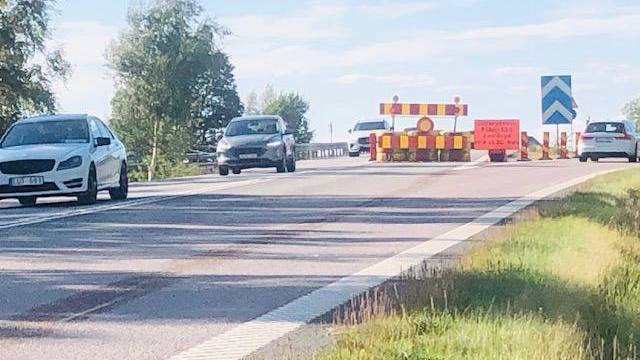 Bilar närmar sig en vägspärr med skyltar och avspärrningar som anger att ett körfält är avstängt en solig dag.
