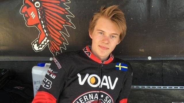 En ung person i en racerdräkt med en svensk flaggmärke sitter framför en vägg med en röd logotyp föreställande en indianhövding och texten ”Indianerna Speedway”.
