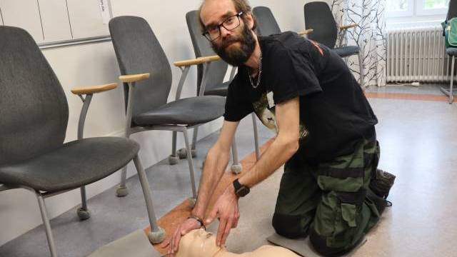 En man står på knä på golvet i ett klassrum och demonstrerar hjärt- och lungräddning på en medicinsk träningsdocka.