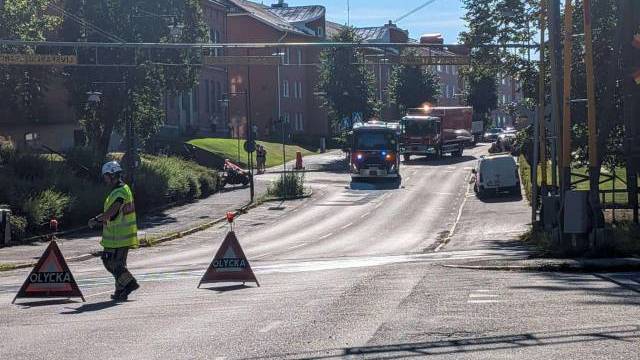 Brandbilar och räddningspersonal spärrar av en gata med varningsskyltar med texten ”Olycka” (olycka) en solig dag i ett bostadsområde.