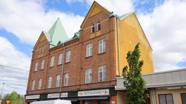En tegelbyggnad med gula accenter och ett grönt tak, med en restaurang på bottenvåningen.