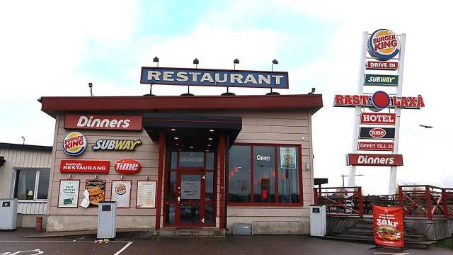 En restaurangbyggnad vid en väg med skyltar för Burger King, Subway, Dinners och Time, och en stor skylt med samma varumärken och hotellinformation.