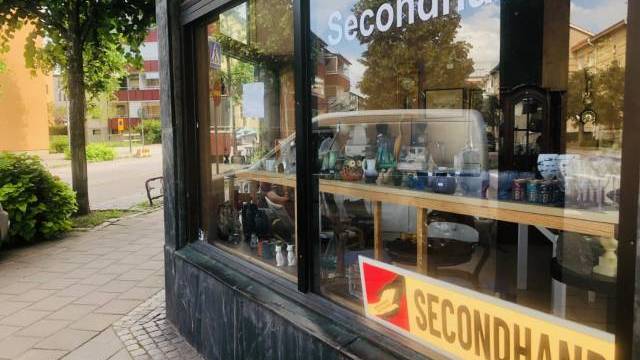 En gatuvy över en secondhandbutik med varor utställda i fönstret och två 