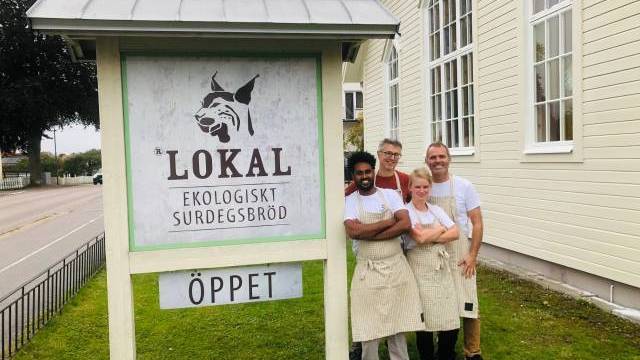 Fyra personer med förkläden står leende framför en skylt för 