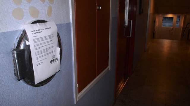 Ett meddelande är fasttejpat på en väggmonterad cirkulär container i en svagt upplyst hall med klinkergolv och dörrar längs väggarna.