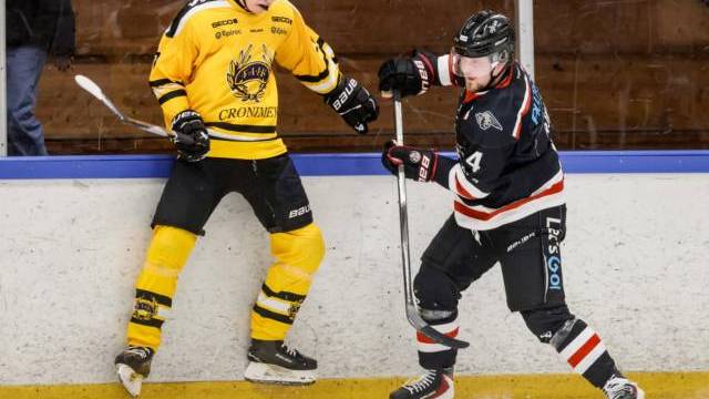 Två ishockeyspelare, en i gult och en i svart, tävlar om pucken nära sargen under en match.
