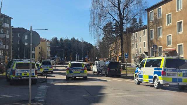 Flera svenska polisfordon står parkerade längs en bostadsgata i dagsljus, med några andra bilar och flerfamiljshus synliga.