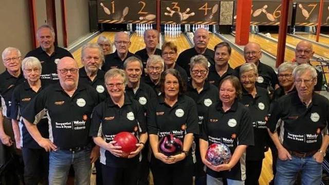 En grupp vuxna i matchande skjortor står tillsammans i en bowlinghall, några håller i bowlingklot och bowlingbanorna syns i bakgrunden.