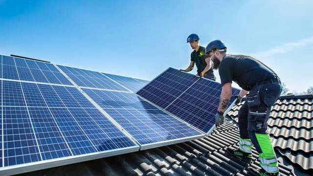 Två män installerar solpaneler på ett tak.