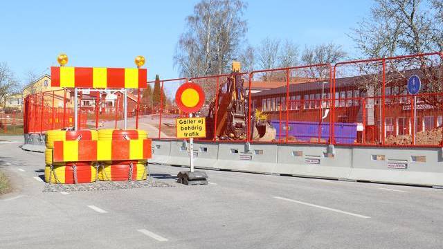 En väg är avstängd med röda och gula bommar, en skylt som begränsar obehörig trafik och byggutrustning som syns bakom stängslet en klar dag.