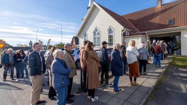 Människor står i en kö utanför en kyrkobyggnad en solig dag och väntar på att få komma in.