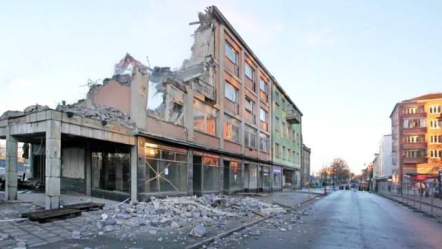 En delvis raserad byggnad med spillror på trottoaren, intill en öde gata i ett stadsområde.