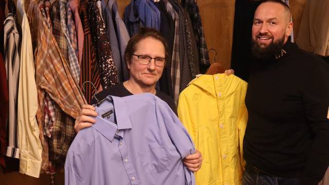 Två män står framför en garderob med kläder; den ene håller i en blå skjorta, den andre håller i en gul regnrock.