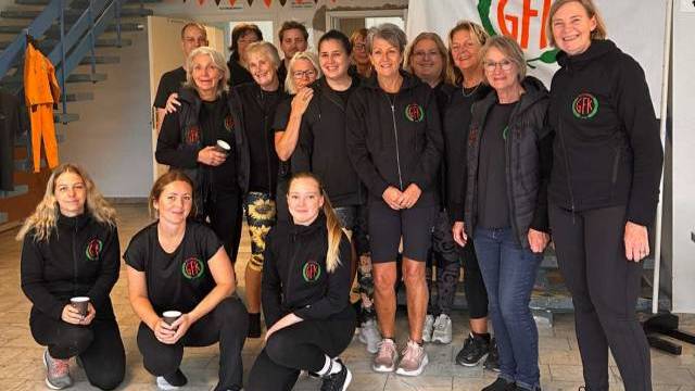 En grupp på tretton kvinnor i svarta träningskläder poserar inomhus framför en banderoll från Ramund GFI.