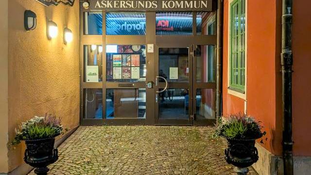 Ingången till Askersunds kommunhus på natten, med krukväxter på båda sidor om en kullerstensgång och upplysta vägglampor.
