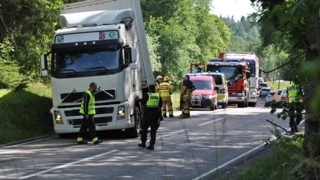 Flera utryckningsfordon och personal rycker ut till en incident med en vit lastbil på en trädkantad väg i dagsljus.