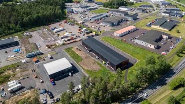 Flygfoto över ett industriområde med flera lagerlokaler, kontor, parkerade fordon, byggarbetsplatser samt omgivande grönområden och vägar.