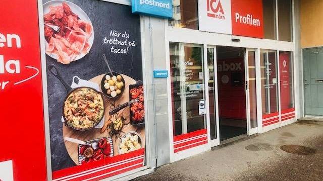 Ingången till en ICA Nära-butik med en stor livsmedelsreklam och skyltar för PostNords posttjänster vid dörren.