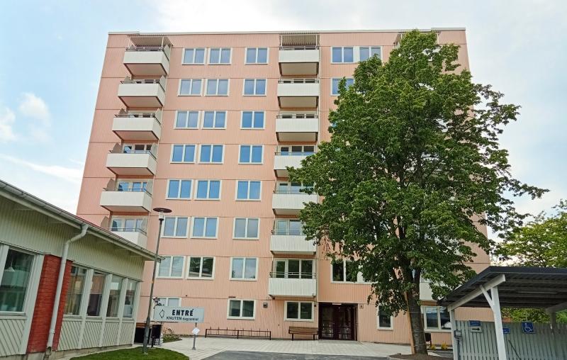 Ett rosa sexvåningshus med balkonger, ett stort träd framför och en skylt med texten 