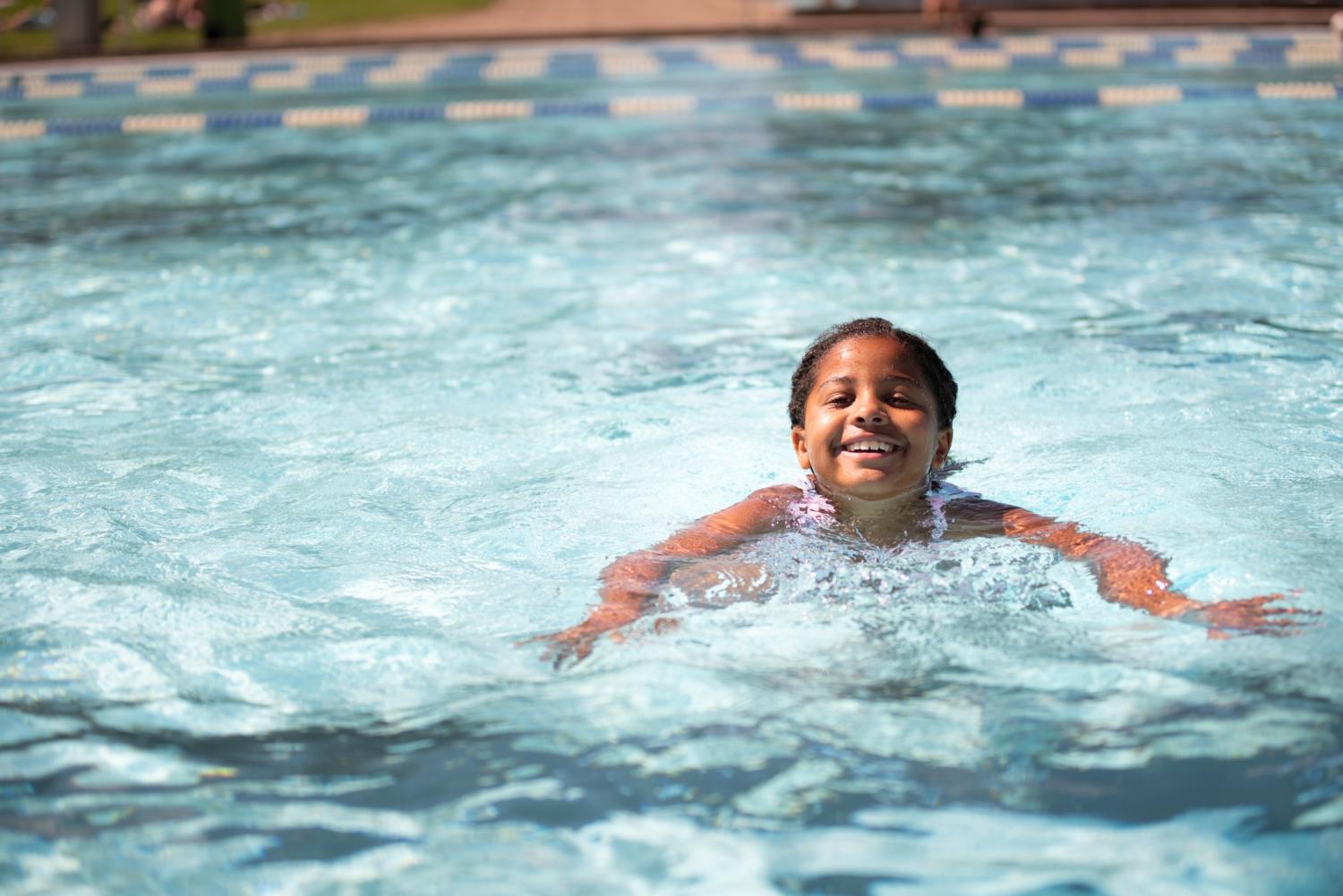Ett litet barn simmar och ler i en utomhuspool en solig dag.