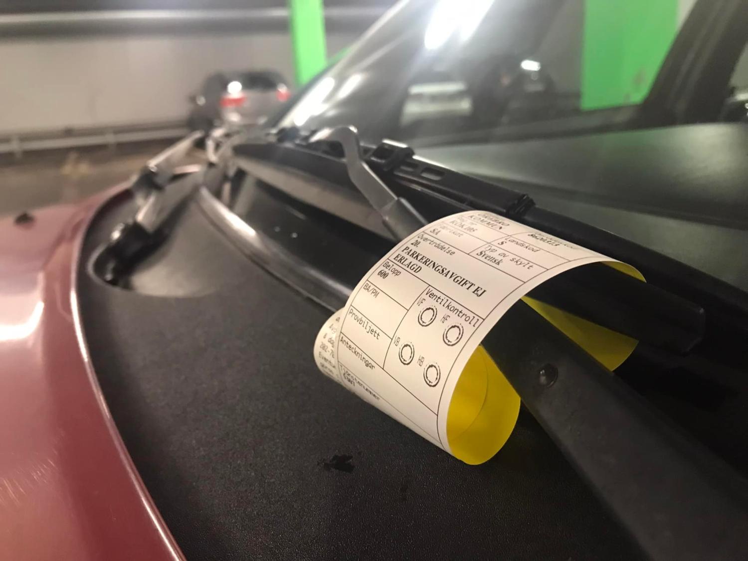 En parkeringsbot placeras under en vindrutetorkare på en röd bil i ett parkeringsgarage.