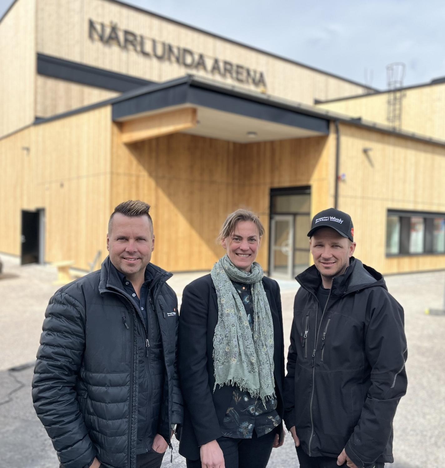 Tre personer ler framför närlunda arena, två män och en kvinna, alla iklädda jackor.