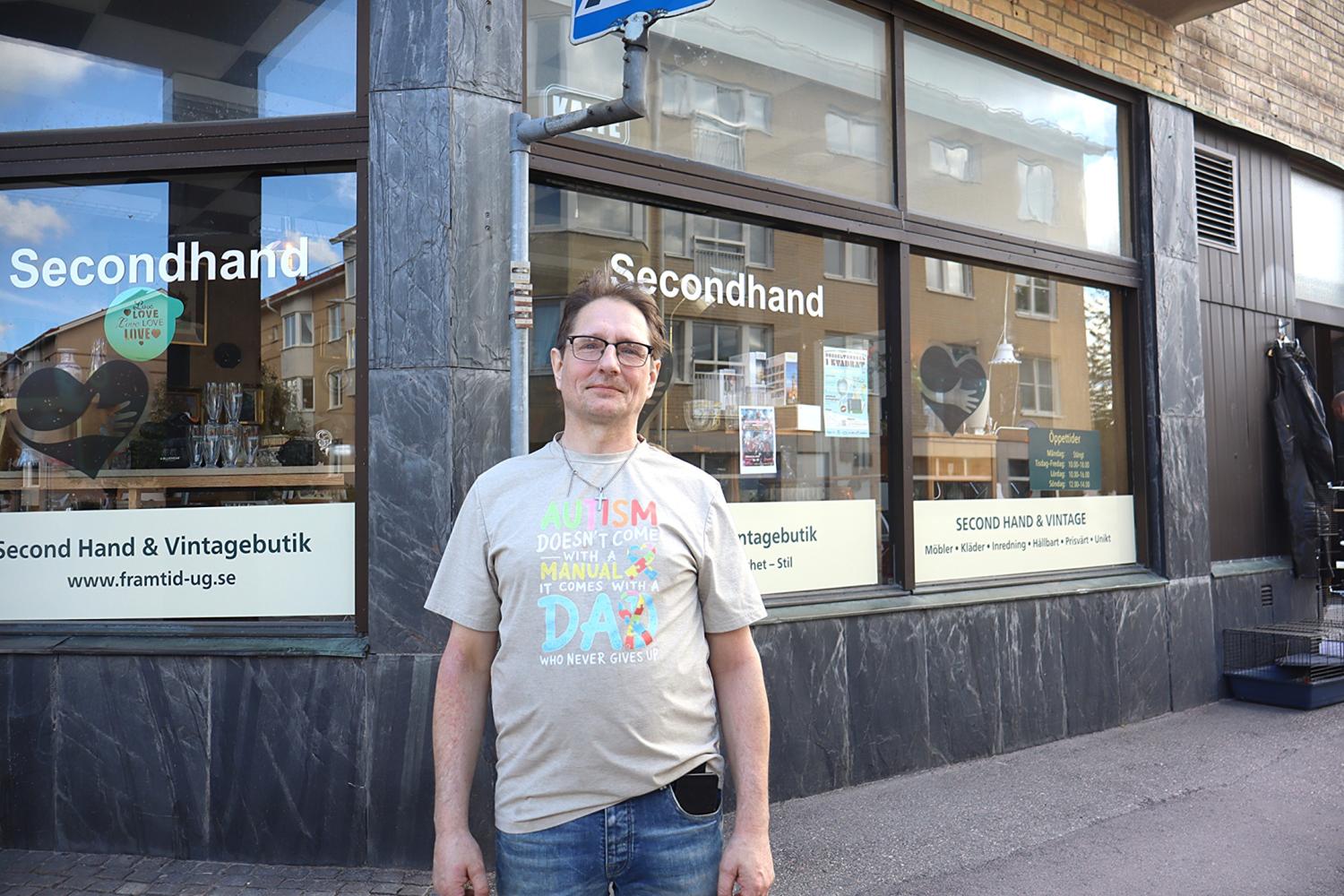 En man står utanför en secondhand- och vintagebutik med stora fönster på en gata i stan.