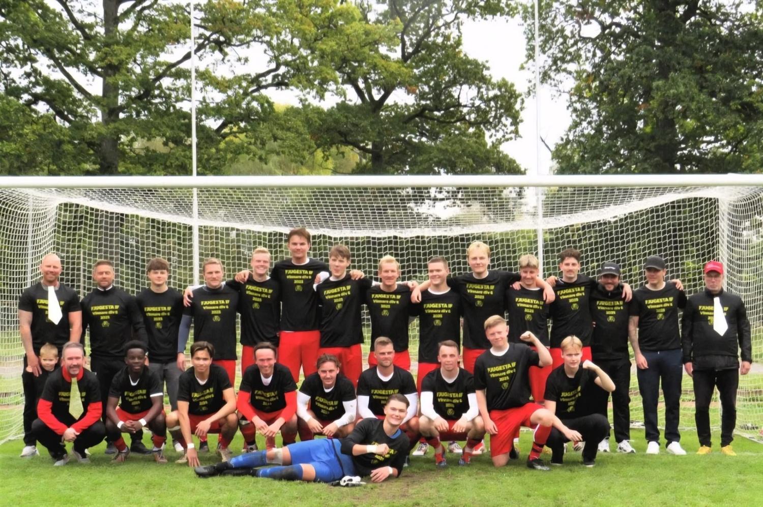 Ett fotbollslag med 22 spelare och 3 tränare poserar framför ett mål på en gräsplan, iklädda matchande svarta tröjor och röda shorts. Två målvakter sitter och ligger framför.