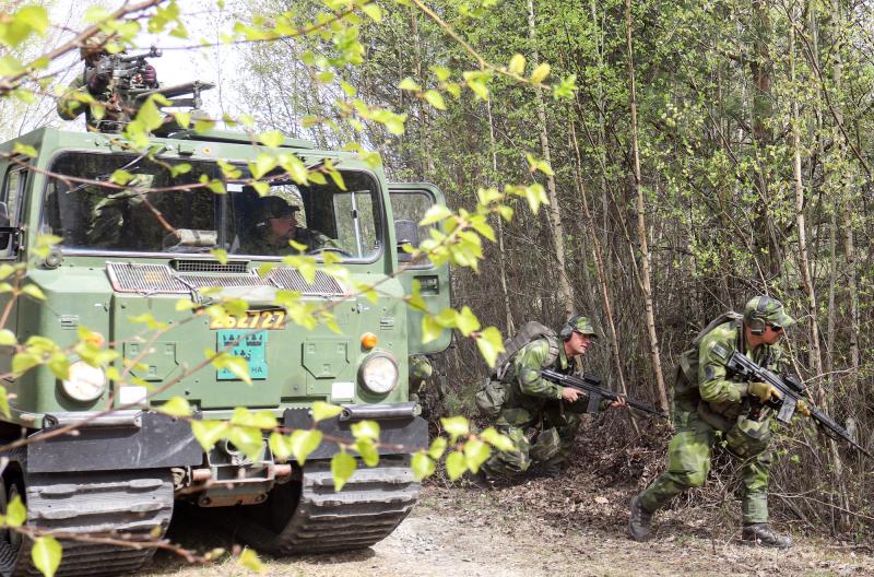 Tre soldater i grön kamouflagedräkt kliver ur ett pansarfordon och rör sig genom ett skogsområde med gevär under en militärövning.