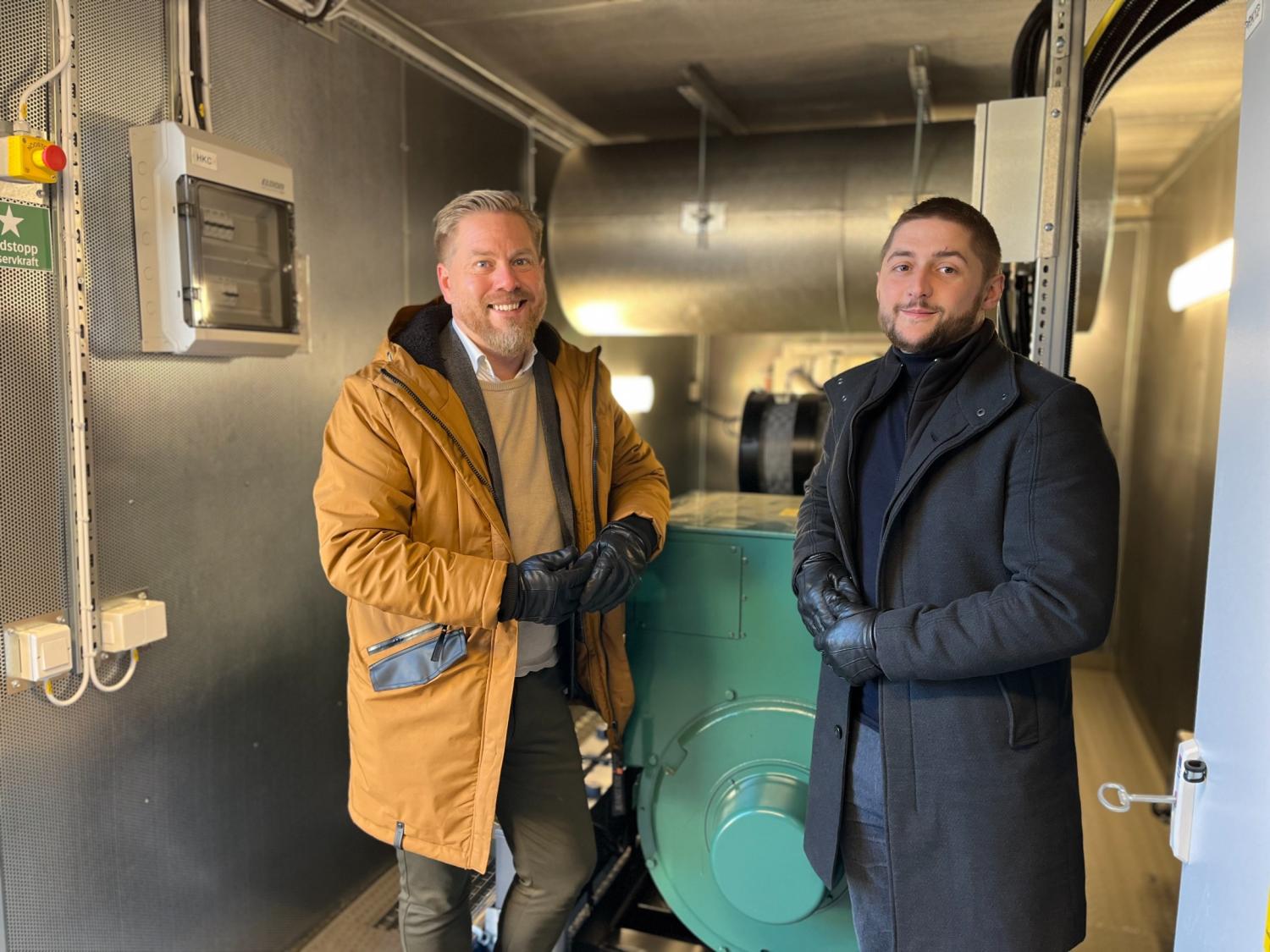 Två män i rockar och handskar står bredvid industriutrustning i en väl upplyst tvättstuga.
