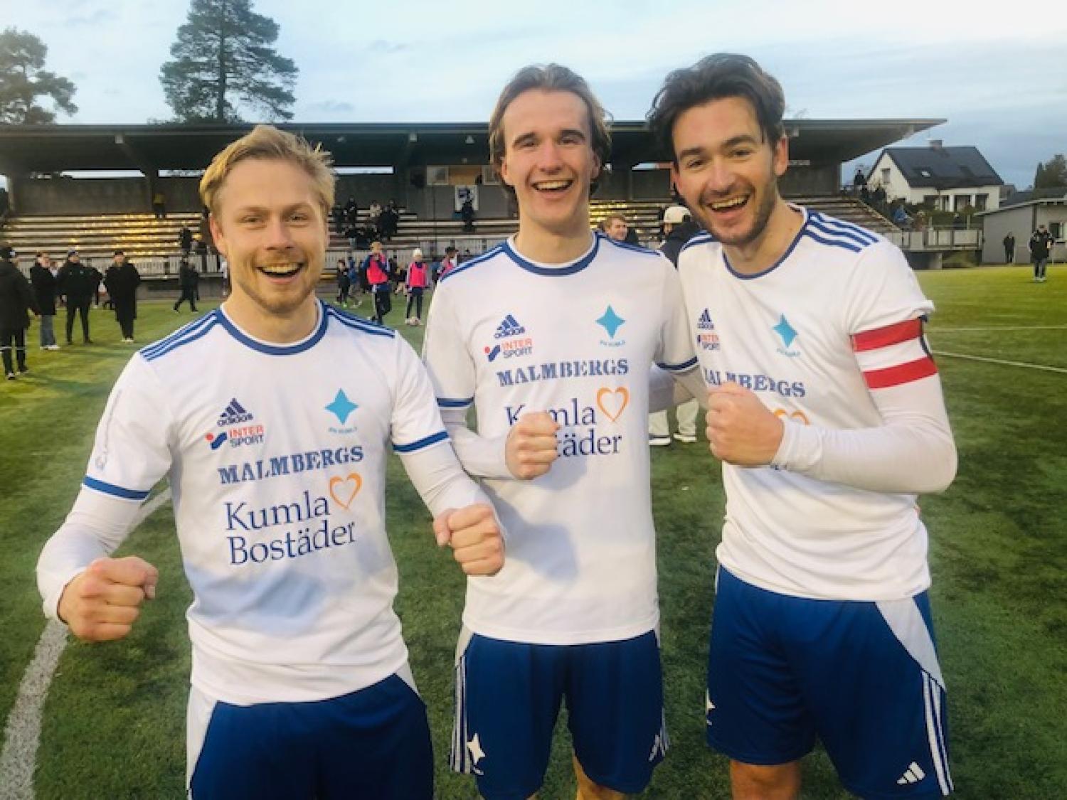 Tre manliga fotbollsspelare i vita tröjor står på en plan och ler och firar, med en stadion och andra människor synliga i bakgrunden.