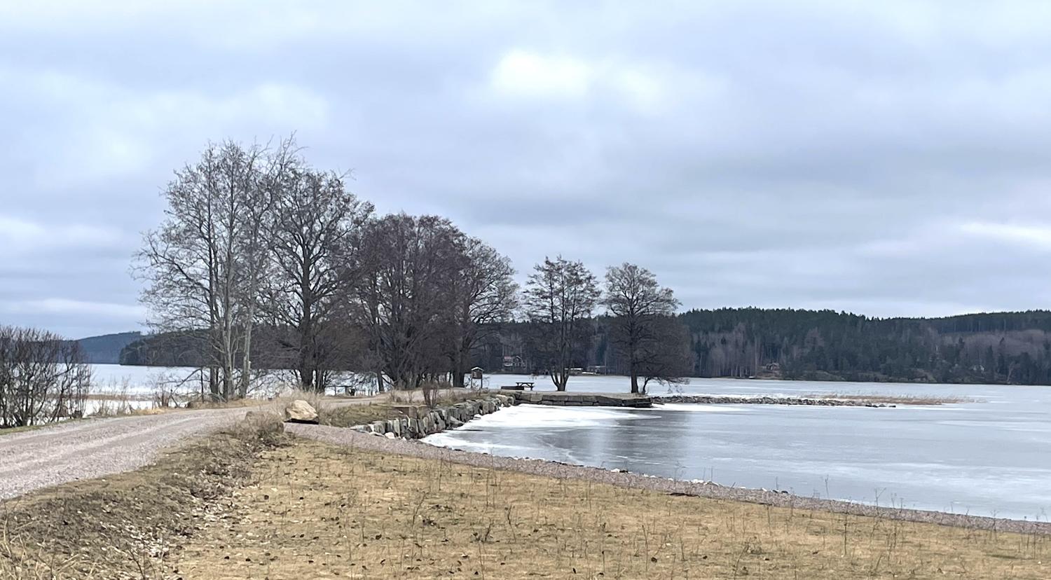 En grusväg bredvid en sjö med is på.