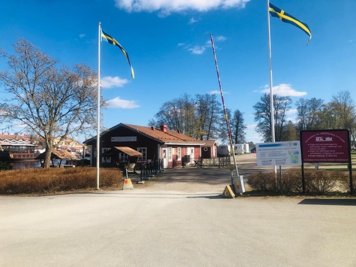 En envåningsbyggnad med uteservering, två svenska flaggor, informationsskyltar och träd under en blå himmel.