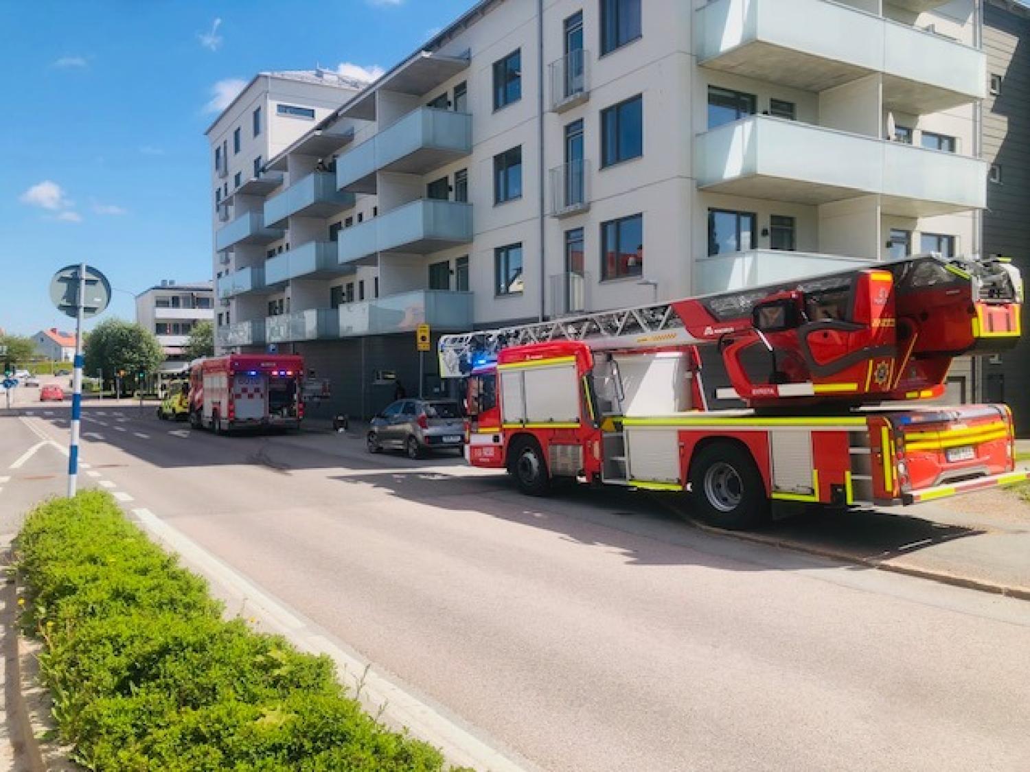 Brandbilar står parkerade på en gata bredvid ett modernt hyreshus, med nödljusen påslagna och utan synlig rök eller lågor.