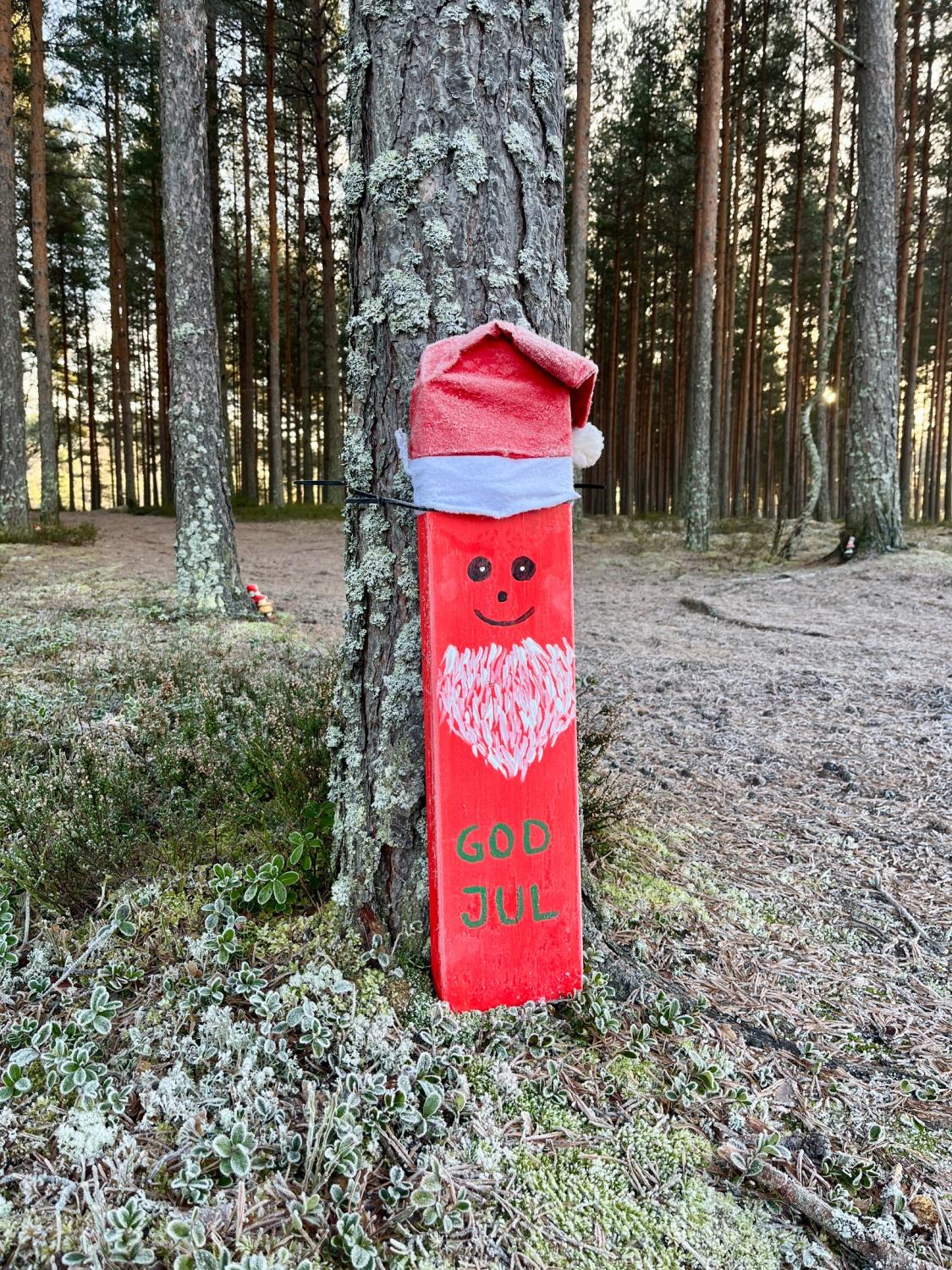 En röd träskiva målad som en tomtefigur med texten 
