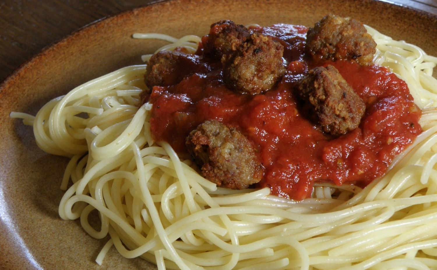 En tallrik spagetti toppad med tomatsås och köttbullar.