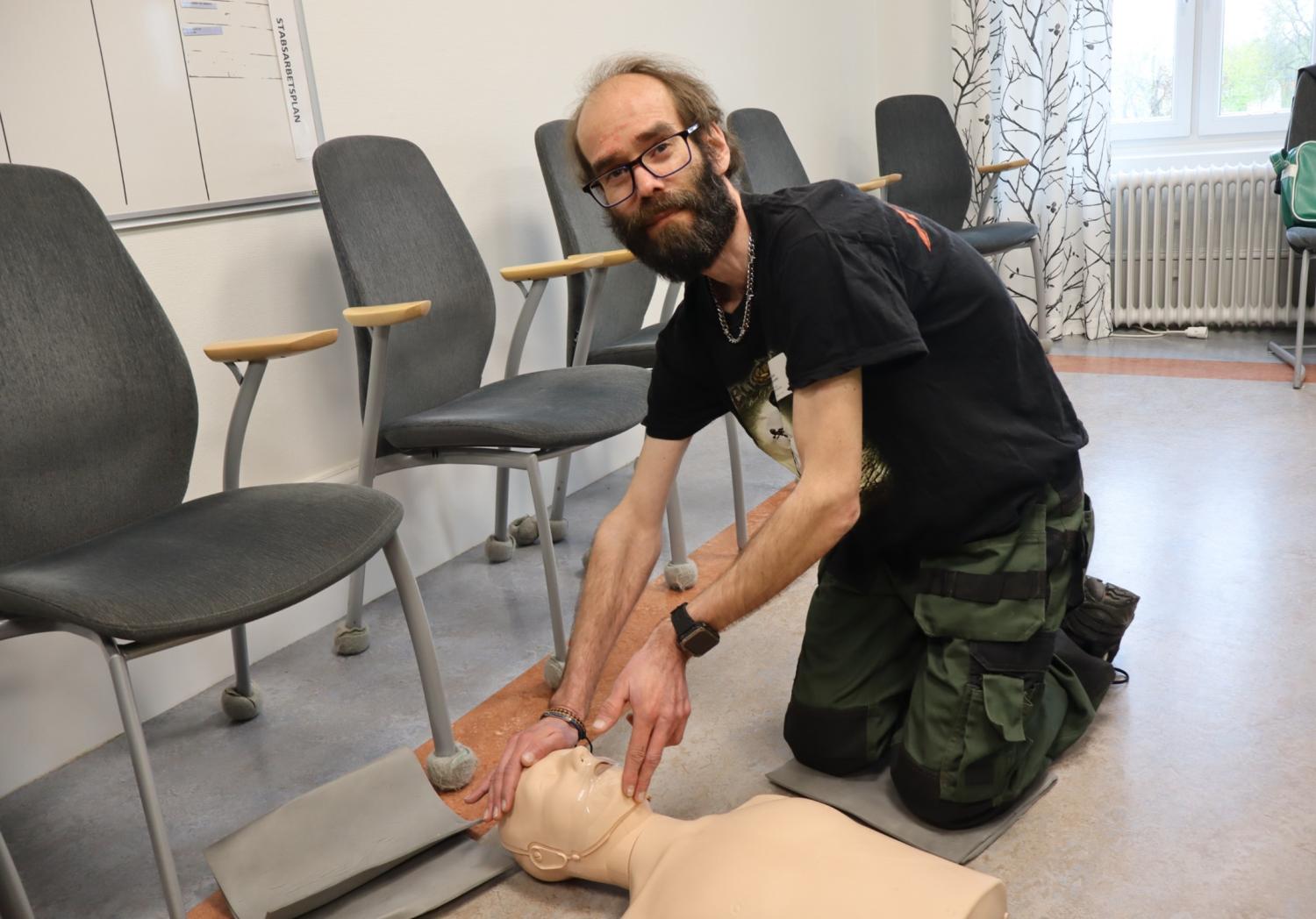 En man står på knä på golvet i ett klassrum och demonstrerar hjärt- och lungräddning på en medicinsk träningsdocka.