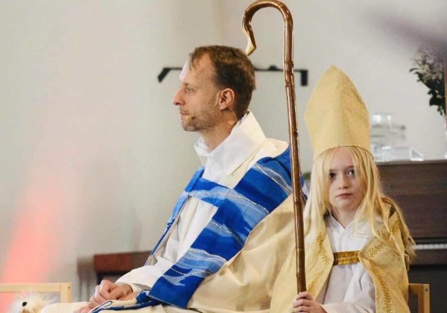 En man klädd i en mantel och en liten flicka som sitter bredvid honom.