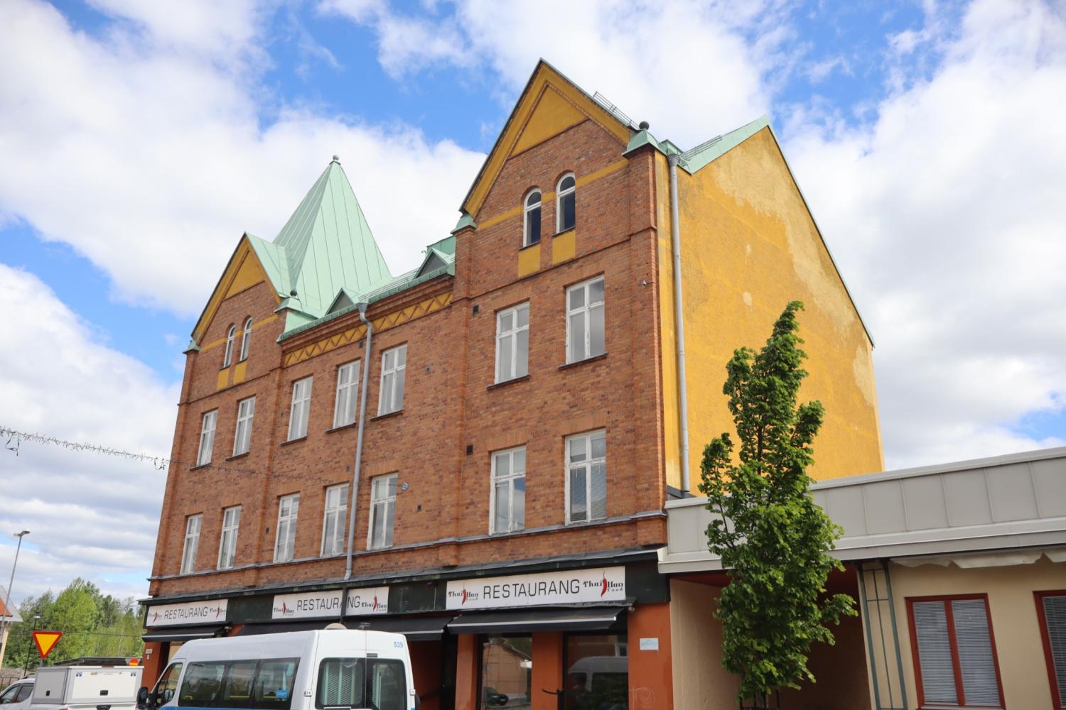 En tegelbyggnad med gula accenter och ett grönt tak, med en restaurang på bottenvåningen.