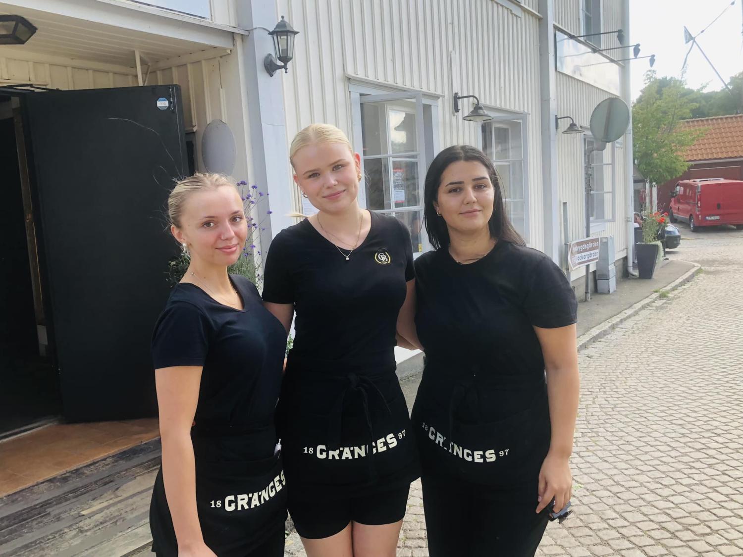 Tre kvinnor klädda i svarta uniformer står utanför en byggnad med 