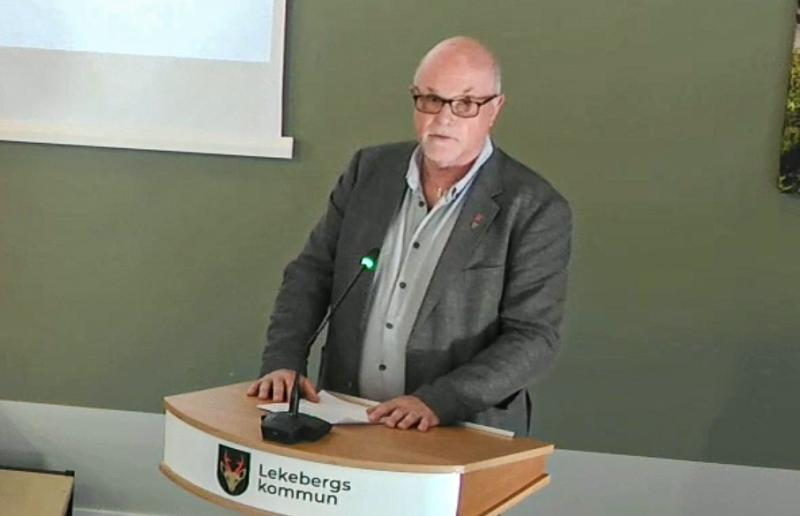 En man i grå kavaj står vid ett podium märkt 