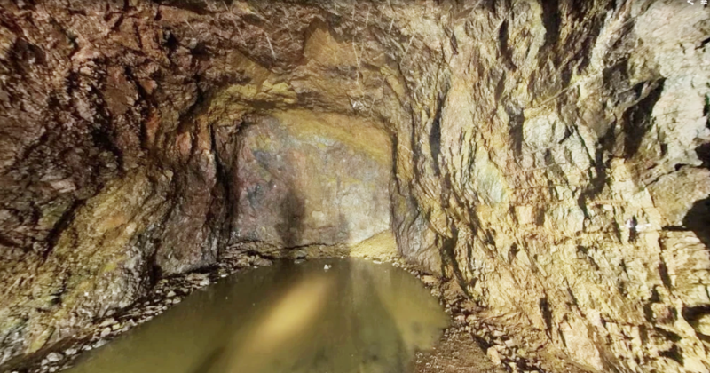 En klippgrotta med grova, ojämna väggar och en grund vattenpöl på golvet. Ljuset kastar skuggor på grottväggarna.