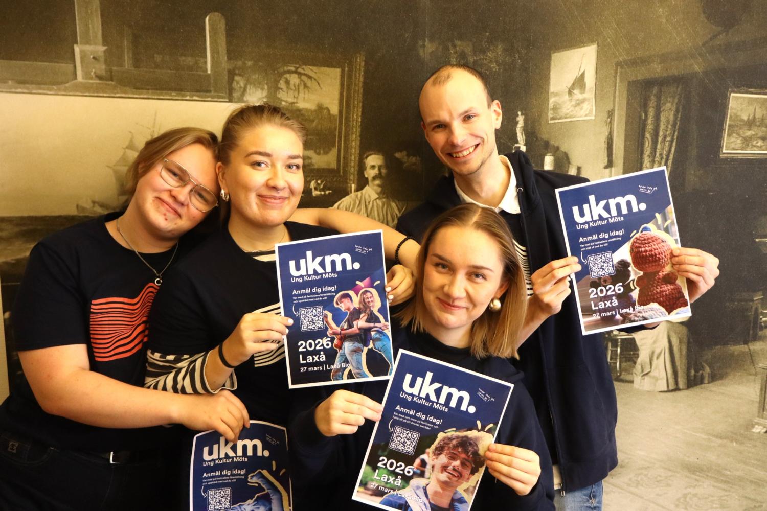 Fyra personer står tätt intill varandra, ler och håller upp blå 