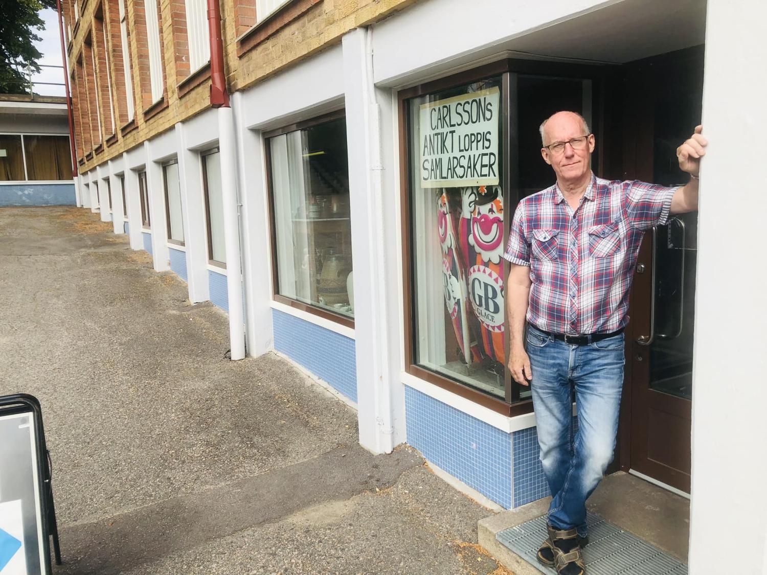 En man i rutig skjorta står i dörröppningen till en skyltfönster märkt 