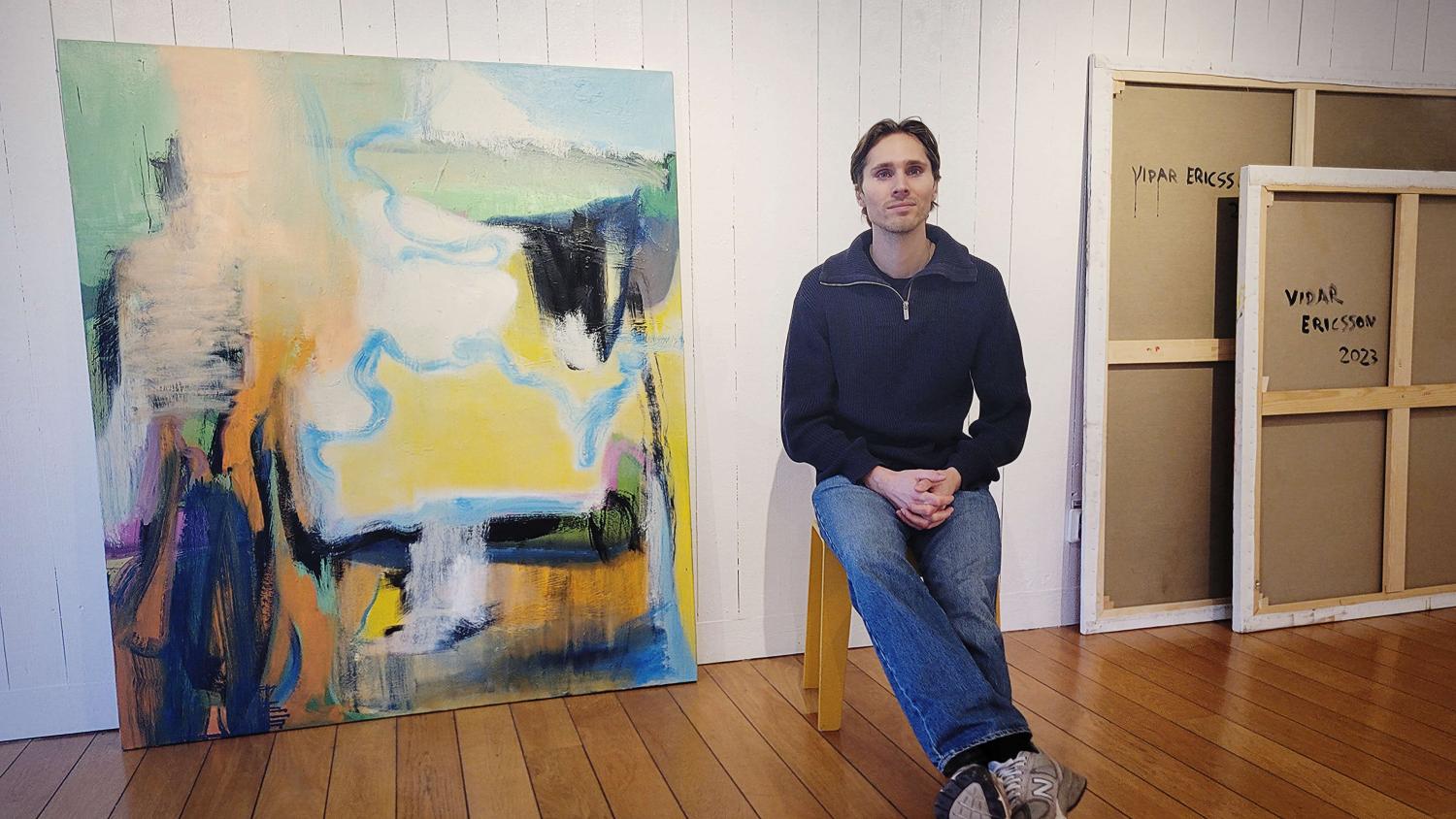 En man som sitter på en stol framför en tavla.