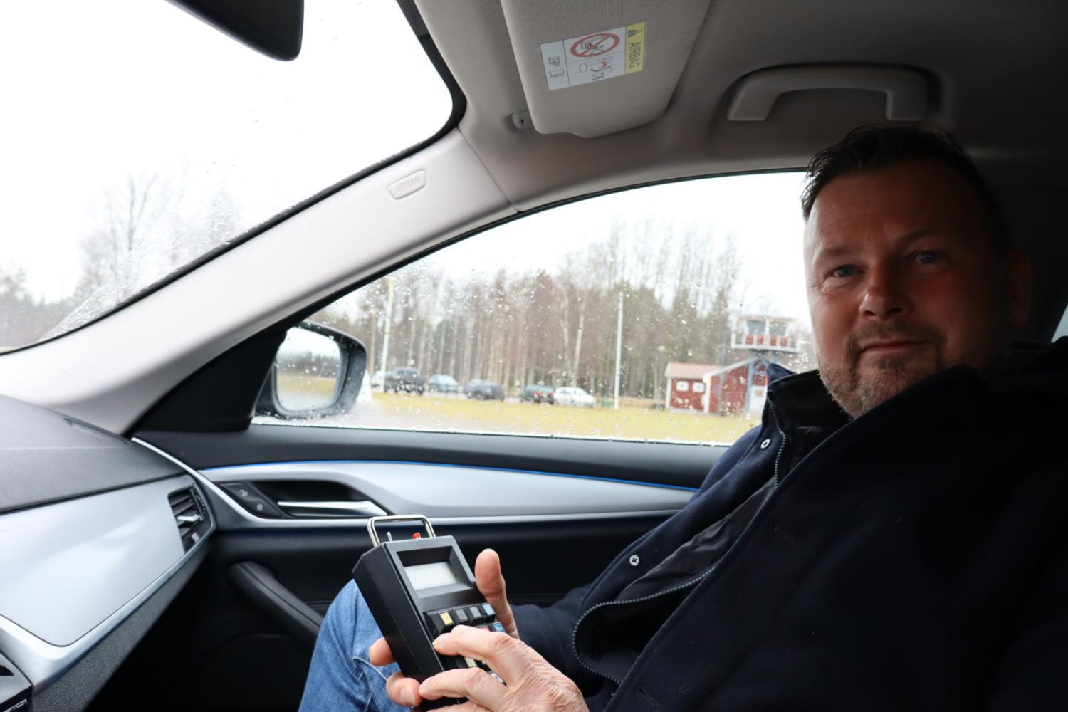 Man sitter i en bil och håller en alkomätare och tittar på kameran.