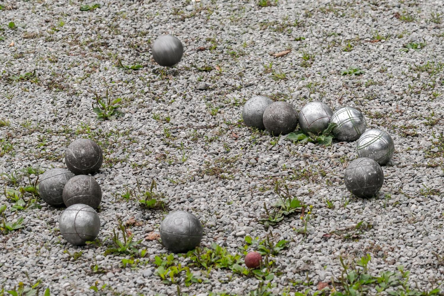 En grupp metallbollar och en mindre målkula ligger utspridda på en grusyta.