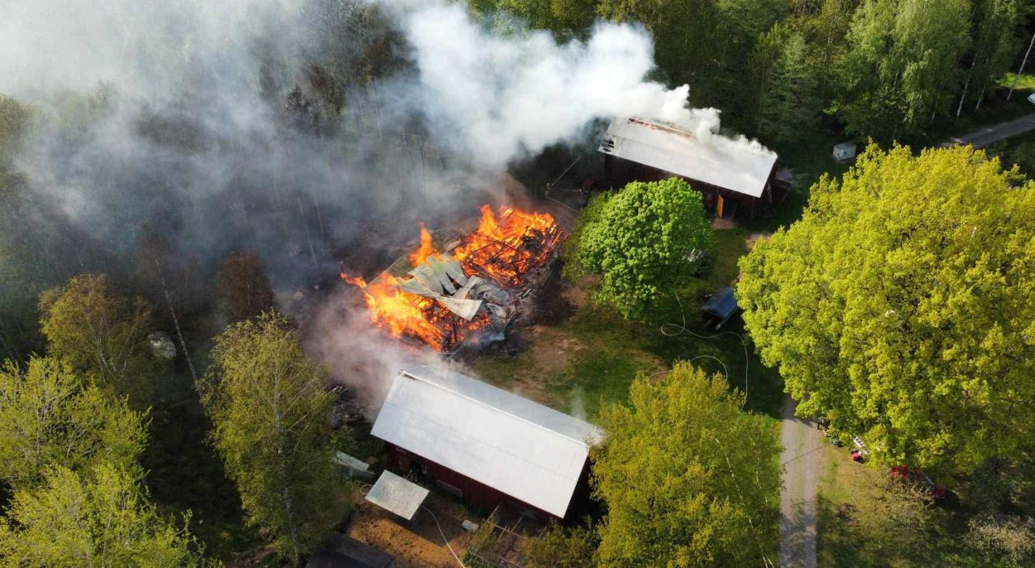 Flygfoto över en brinnande byggnad omgiven av träd, med tjock rök som stiger upp och närliggande strukturer oskadade.